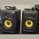Dva černé studiové monitory s žlutými membránami basových reproduktorů. Na přední straně každého reproduktoru je logo KRK a nápis ROKIT 6. K oběma př…