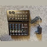 Černý kompaktní mixážní pult s nápisem Mix8 8-CHANNEL COMPACT MIXER a doprovodným logem. Zařízení obsahuje různé vstupy, potenciometry pro Gain, EQ,…