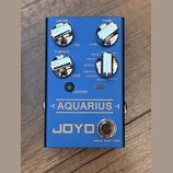 Modrý efekt pedál s nápisy AQUARIUS a JOYO. Na horní části jsou čtyři chromované ovládací knoflíky s popisky LEVEL, TIME, F.BACK a TAPE. U pravého kn…