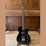 Černý elektrický basový kytara s tmavým hmatníkem. Na hlavě je zlatý nápis GRETSCH a na korpusu v pravé dolní části bílý nápis GRETSCH. Nástroj má dv…