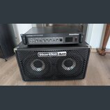 Černý basový zesilovač Hartke LH1000 1000 WATT BASS AMPLIFIER CLASS A VALVE PREAMP položený na černém basovém reproduktoru Hartke HL210 HyDrive. Zesi…