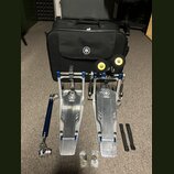 Sada kovových bubnových pedálů v modré a stříbrné barvě s logem YAMAHA. Součástí je černá přepravní taška s bílým logem Yamaha, dvě žluté gumové podl…