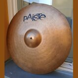 Kovový činel v bronzové barvě s viditelným koncentrickým rýhováním povrchu. V horní části je modré logo pAiste a pod ním menší nápis 20 RIDE. Povrch…