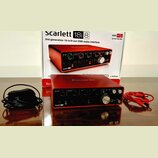 Červená USB audio rozhraní Focusrite Scarlett 18i8 s kovovým povrchem. Na přední straně jsou vidět regulační knofíky, přepínače a konektory. Vedle za…