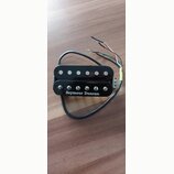 Černý humbucker s kovovými póly a bílým nápisem Seymour Duncan. Nástroj má připojený kabel s několika barevnými vodiči. Povrch je lesklý a vykazuje m…