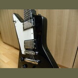 Černá elektrická kytara s bílým pickguardem a dvěma humbuckery. Na krytcích snímačů nejsou žádné viditelné nápisy ani loga. Povrch kytary je glossy,…