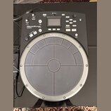 Černý elektronický perkusní pad značky Roland. Na zařízení je nápis HANDSONIC Expr/NATURAL a označení modelu HPD-20. Horní část obsahuje displej, ovl…