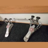 Dvojpedál na buben v kovovém provedení stříbrné barvy. Na obou stupňech je vidět červenobílý kulatý štítek s nápisem SONOR GERMANY SINCE 1875. Povrch…