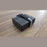 Černý obdélníkový box s žebrovaným horním povrchem a řadou deseti vstupních konektorů. Na boku jsou pod konektory viditelna čísla 1 až 10. Box je omo…