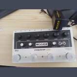 Bílý kytarový předzesilovač s černým ovládacím panelem a značkou MOOER. Na panelu jsou popisky VOL, BASS, MID, TREBLE, GAIN, MASTER, PRESENCE a FX LE…