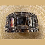 Stříbrný chromovaný snare drum s kovovým korpusem a chromovaným kováním. Uprostřed korpusu je umístěn malý čtvercový štítek s modrým nápisem SONOR. P…