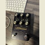 Černý kytarový předzesilovač s kovovým šasi a zlatými ovládacími knoflíky. Na předním panelu jsou nápisy LION 68 SUPER LEAD AMP, BASS, MIDDLE, TREBLE…