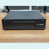 Černý kovový přístroj s hranatým tvarem. Na přední straně je nápis UAD-2 Satellite a displej s logem UA a textem UNIVERSAL AUDIO a HOST. Povrch je ma…