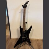 Černá elektrická kytara s ostře hranatým korpusem umístěná na stojanu. Na hlavě hmatníku je bílé logo Jackson. Nástroj má dva humbuckery, z nichž na…