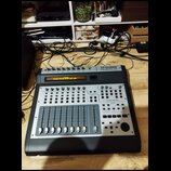 Černý kontrolér s kovovým horním panelem. V pravém horním rohu je nápis M-AUDIO PROJECTMIX I/O. Displej zobrazuje text M-Audio Control Surface is in…