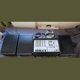 Sada zvukové soustavy tvořená třemi černými reproduktory s mřížkami a mixážním pultem v přepravním kufru. Na pultu je nápis PORTABLE POWERED MIXER a…