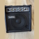 Černý kombo zesilovač s kovovou mřížkou reproduktoru, na které je bílé logo Laney. Horní ovládací panel obsahuje nápisy MIC/LINE, LEVEL, LINE/INST, D…