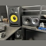Na fotografii jsou tři studiové monitory a jeden mixér. Největší černý reproduktor má žlutý membránový basový reproduktor a nápisy KRK a ROKIT 8. Ved…