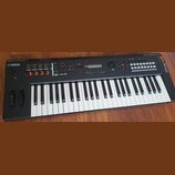 Černý klavírní syntetizátor s bílými a černými klávesami. Na levé straně je nápis YAMAHA a na pravém okraku svisle napsáno 64xw. V horní části panelu…