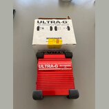 Červená DI box s hliníkovým žebrovaným povrchem a černými gumovými nohami. Na zařízení je bílý nápis ULTRA-G, logo BEHRINGER a text ACTIVE DI-BOX/VIR…