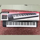 Fotografie zobrazuje černý klaviaturní kontrolér M-AUDIO KEYSTATION 61 MK3 a jeho původní kartonovou krabici. Na přístroji i na obalu je vidět značka…