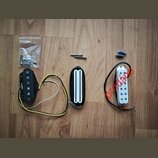 Tři elektrické snímače na kytaru v černé barvě. Jeden je s černým plastovým krytem a viditelnými póly, druhý má bílé plastové kryty v řadě a třetí je…