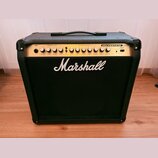 Černý kytarový kombozesilovač s látkovým předním krytem a zlatým ovládacím panelem. Na přední straně je bílý nápis Marshall a v pravém horním rohu oz…