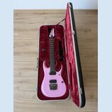 Růžová elektrická kytara v tvrdém kufru s červeným polstrováním. Na hlavě hmatníku je bílý nápis Ibanez. Kytara má dva humbuckery, Tremolo most a čer…
