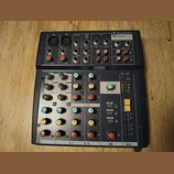 Černý mixovací pult značky Soundkraft, model Notepad 12 FX. Zařízení obsahuje několik vstupních kanálů s otočnými knoflíky v oranžové, žluté a modré…