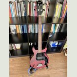 Čtyřstrunná basová kytara s červeným trupem a hnědým hmatníkem. Na hlavě je zlaté logo Gibson a nápis Gibson Custom Shop. Instrument má černý pickgua…