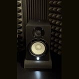 Černý studiový monitor v hranaté skříni, umístěný na černém podstavci. Reproduktor má v horní části malý výšek s mřížkou a ve spodní části větší bílý…