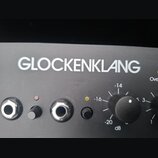 Detailní pohled na černý panel hudebního zařízení s bílým nápisem GLOCKENKLANG. Jsou vidět dva ovládací knoflíky, dvě zásuvky a dvě kontrolní LED dio…