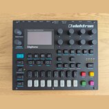 Černý polyfonní digitální syntetizátor s nápisem Elektron v pravém horním rohu a označením Digitone pod displejem. Nad displejem je text Polyphonic D…