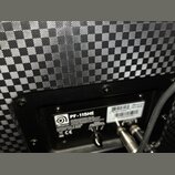 Detail zadní strany reproduktoru s černým šachovnicovým potahem. Na černé plošce je bílý nápis PF-115HE a logo s názvem Ampeg. Jsou zde uvedeny speci…