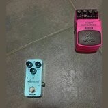 Na fotografii jsou dva efektové pedály umístěné na šedém povrchu. Jeden je růžový s nápisy OUT, IN, HEAVY DISTORTION, HD300 a logem behringer. Druhý…