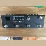 Černý kytarový spínací pedalboard s nápisy MOEN a GEC 5 Guitar Effect Commander. Zařízení má čtyři spodní spínače označené čísly 1, 2, 3 a 4 s doplňk…