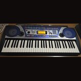 Elektronický klavír v černé barvě s modrým ovládacím panelem a dvěma integrovanými reproduktory po stranách. Na panelu je viditelné logo YAMAHA a ozn…