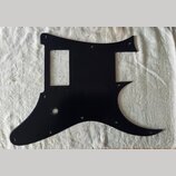 Černý plastový pickguard pro elektrickou kytaru s výřezem pro ovladače a otvorem pro kabel. Povrch je hladký a bez viditelných značek, log nebo nápis…