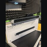 Na fotografii je stříbrno-černý rackový audio rozhraní s řadou 16 XLR konektorů. Zařízení leží na bílé krabici s nápisy StageCONNECT, DN4816-O a text…