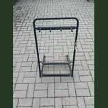 Černý kovový stojan na hudební nástroje s horní lištou vybavenou čtyřmi kolíky. Na pravém bočním sloupeku je viditelný bílý nápis th.mann. Povrch sto…