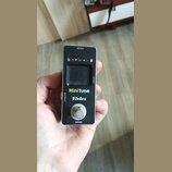 Černý kytarový ladič v kompaktním kovovém provedení. Na přední straně je displej, tři kontrolky a nápisy MiniTune a Vivlex. V horní části je označení…