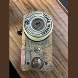 Kytarový efekt s bílým ovládacím knoflíkem a šasi z texturovaného materiálu v hnědo-šedých tónech. Na knoflíku je nápis BY SALVATION AUDIO TONE WHEEL…