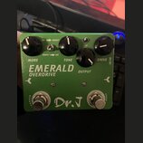 Zelený kytarový efekt s nápisy EMERALD OVERDRIVE a Dr. J. Na horní straně jsou čtyři černé otočné knoflíky s popisky MORE, TONE, OUTPUT a DRIVE. Mezi…