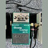 Zelený efekt pedál značky BOSS s nápisy Bass Comp a BC-1X. Na horní části jsou čtyři ovládací knoflíky s popisky LEVEL, ATTACK, RATIO a Tone, pod nim…