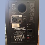 Zadní strana černého studiového monitoru. Je na něm vidět logo M-AUDIO a název modelu STUDIOPHILE BX5a DELUXE, v horní části je velký nápis BX5a DELU…