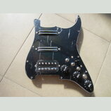Černý plastový pickguard pro elektrickou kytaru s třмя snímači. Horní dva jsou humbuckery s chromovaným krytem, spodní je singl v průhledném plastové…