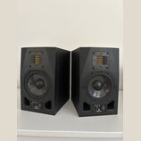 Dva černé studiové monitory v plastovém nebo lakovaném provedení. Každý reproduktor má v horní části žlutý páskový výšek a ve spodní části kruhový ba…