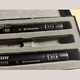 Dvě černá kondenzátorová mikrofony umístěná v šedém pěnovém pouzdře. Na obou je bílý nápis SENNHEISER s doprovodným logem a červený přepínač s nápise…