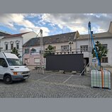 Fotografie zachycuje venkovní instalaci kovového hliníkového truss systému s černou plátnem v pozadí. Konstrukce je zajištěna modrými napínacími popr…