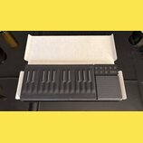 Černý MIDI kontrolér s gumovou klávesnicí a doprovodným touchpad-padem v bílém kartonovém obalu. Zařízení obsahuje řadu vyvýšených kláves s bílými vo…
